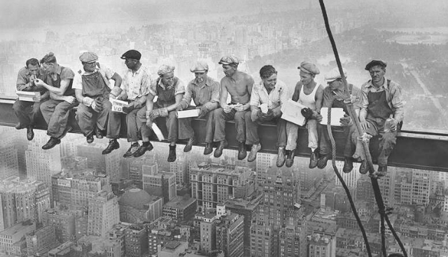 Black and white photo of men eating lunch on a skyscraper beam in New York.