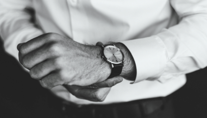 Black and white photo of a man in a white shirt putting on a watch.