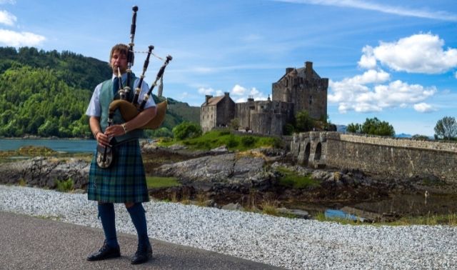 Man with Scottish ancestry playing bagpipes in front of castle