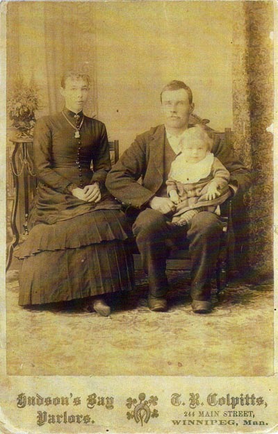 Portrait of a mother, father and baby in the 1800s. The bottom reads "Hudson Bay Parlors" and lists the name of the photographer, as well as an address.