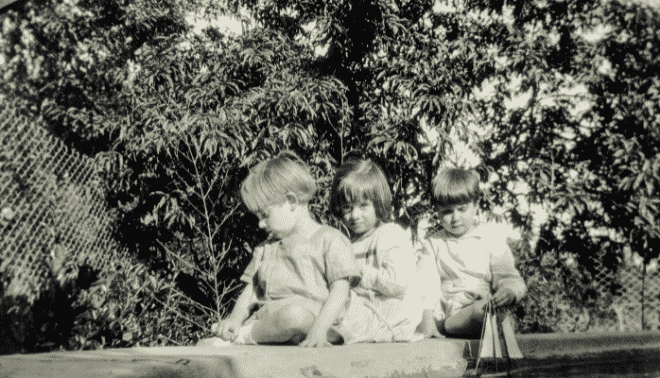 Vintage photo of three children sitting on a garden wall with a toy sailboat.
