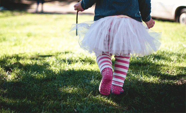 Young child taking small steps across a green lawn.