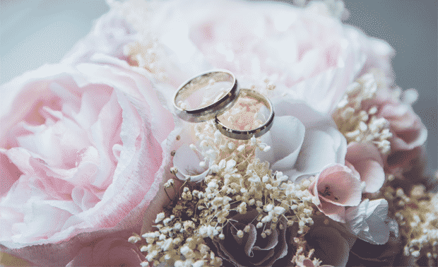 Two wedding rings laying on top of a bouquet of pink flowers.