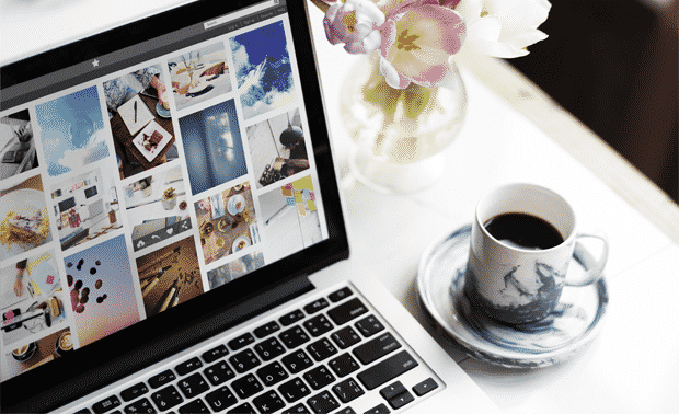 Open laptop showing organized digital photos next to vase of flowers and coffee mug.