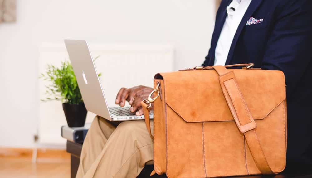 Man in professional dress working on a laptop next to a leather briefcase.