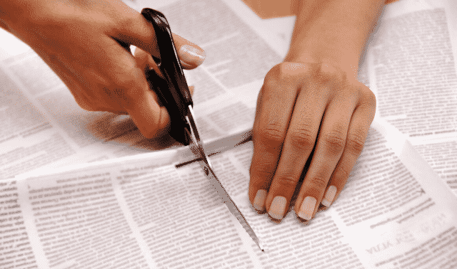 A person cutting out newspaper clippings with scissors.