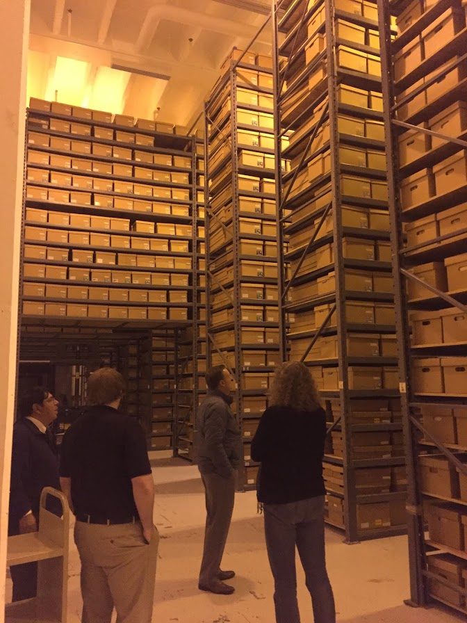 FamilySearch staff and local archivists survey tall shelves that contain several boxes of genealogy records at the Minnesota State Archives