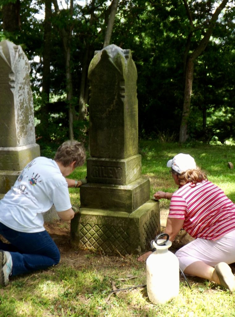 Two women cleaning a headstone.