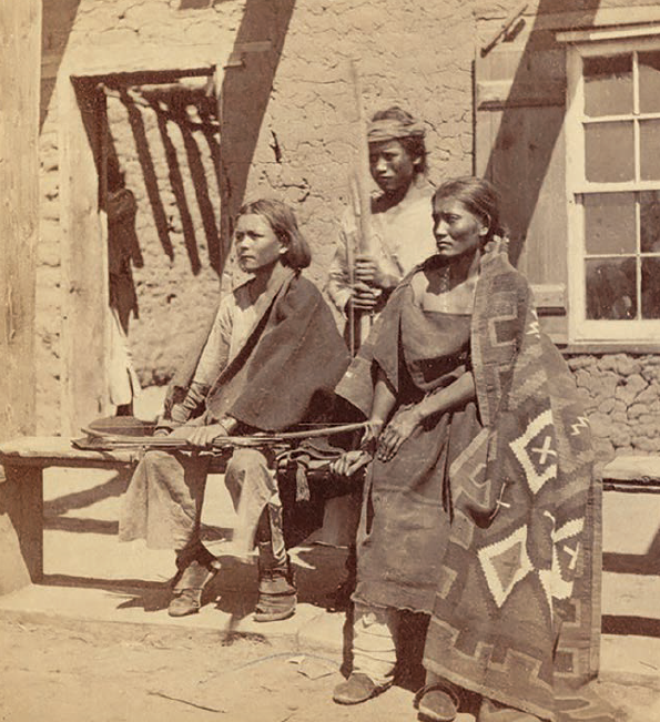 Group of three Navajo sitting together outside a building.